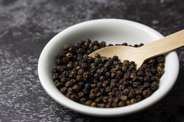 Black pepper in a bowl on dark background.