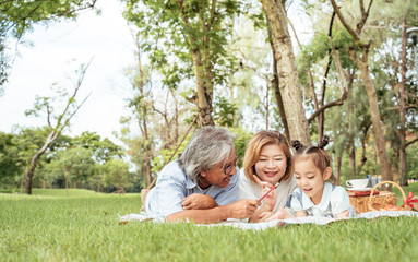 Naklejka premium Grandmother,Grandfather and grand daughter enjoying sunny garden holiday together, outdoors space, leisure lifestyle,happy teaching with flare light sky in park.