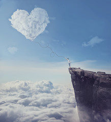 Imaginary view with a boy on the edge of a cliff, trying to catch a heart shaped cloud with a long...