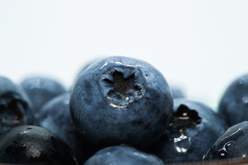 Macro closeup photo of blueberries laying on top of each other in a plate washed with fresh water and with reflection of ambient light.