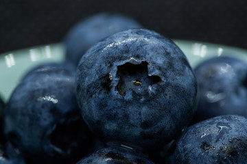 Macro closeup photo of blueberries laying on top of each other in a plate washed with fresh water and with reflection of ambient light.