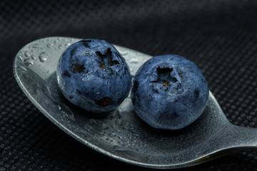 Blueberries Macro close-up photo of stacked and side by side in a teaspoon on a dark background covered with small drops of water.
