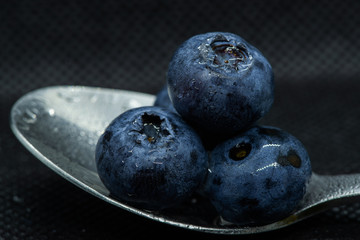 Blueberries Macro closeup photo of superimposed on top of each other and tiled in a teaspoon on a dark background glistening in drops of fresh water.