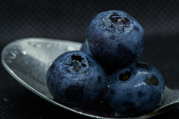 Blueberries Macro close-up photo of stacked and side by side in a teaspoon on a dark background covered with small drops of water.