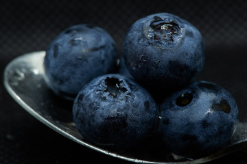 Blueberries Macro close-up photo of stacked and side by side in a teaspoon on a dark background covered with small drops of water.