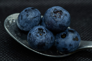 Blueberries Macro closeup photo of superimposed on top of each other and tiled in a teaspoon on a dark background glistening in drops of fresh water.