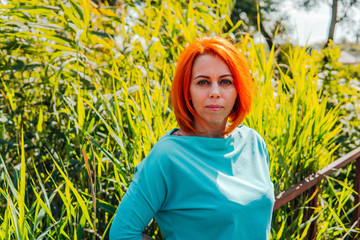 Portrait of an adult red-haired woman in casual clothes is standing on the bridge