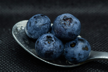 Blueberries Macro closeup photo of superimposed on top of each other and tiled in a teaspoon on a dark background glistening in drops of fresh water.