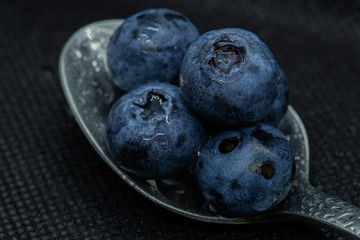 Blueberries Macro close-up photo of stacked and side by side in a teaspoon on a dark background covered with small drops of water.