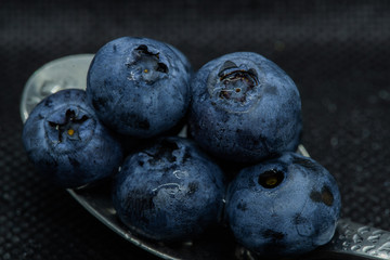 Blueberries Macro closeup photo of superimposed on top of each other and tiled in a teaspoon on a dark background glistening in drops of fresh water.