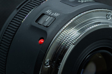 Macro closeup photo of lens to dslr camera on dark background view of red dot and silver extension ring and autofocus button.