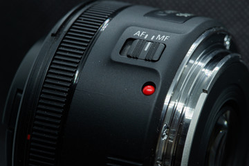 Macro closeup photo of lens to dslr camera on dark background view of red dot and silver extension ring and autofocus button.