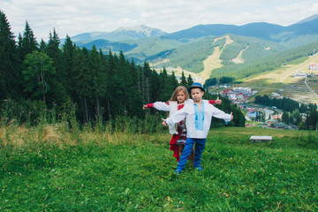 Fototapeta na wymiar Brother and sister in national clothes in the mountains. Children travel. Beautiful boy and beautiful girl smiling in nature