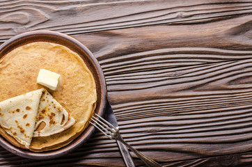 Flat lay view at Stack of French crepes with butter in ceramic dish on wooden kitchen table
