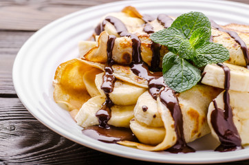 French crepes with chocolate sauce and banana in ceramic dish on wooden kitchen table