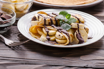 French crepes with chocolate sauce and banana in ceramic dish on wooden kitchen table