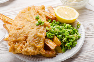 Traditional British street food fish and chips with tartar sauce and mushy peas on paper plate
