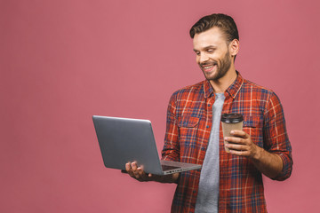 Portrait of young man in casual standing against pink background with copy space for ads, holding laptop with happy smile. Drinking coffee or tea.