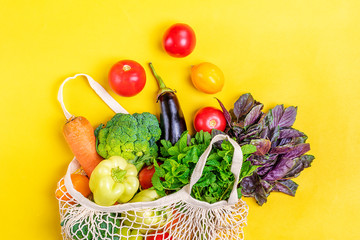 Eco friendly mesh shop bag with organic green vegetables on yellow background. Flat lay, top view. Zero waste, plastic free concept. Healthy clean eating diet and detox concept