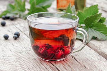 A cup of tea with black currants on a wooden table next to green leaves and currant berries.