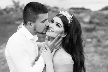 Young happy smiling cheerful attractive couple celebrating outdoor. Man with a beard kissing his girlfriend and looking at her. Beautiful brunette girl with a perfectly curly hair. Black and white.
