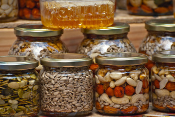 Lots of assorted honey on the table. Jars of sweets are sold at the fair. Honey with different kinds of nuts then dried fruits.