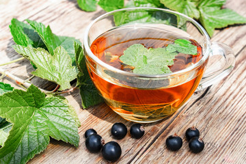 A cup of tea with black currant leaves. Tea with currants on a wooden table.