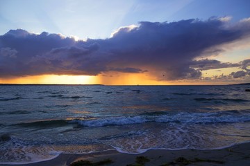 Dramatic sunset through a cloudy dark sky over the ocean.