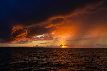 Fototapeta na wymiar Dramatic sunset through a cloudy dark sky over the ocean.