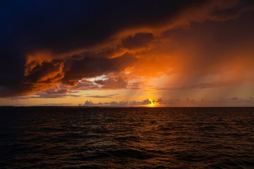 Fototapeta na wymiar Dramatic sunset through a cloudy dark sky over the ocean.