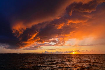Dramatic sunset through a cloudy dark sky over the ocean.