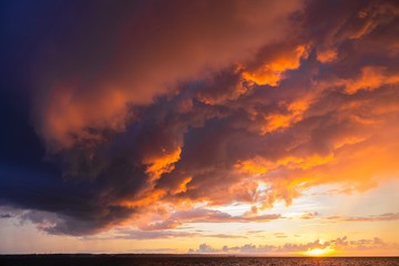 Dramatic sunset through a cloudy dark sky over the ocean.