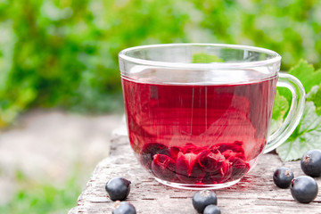 Glass cup of fruit tea with black currant berries on a wooden table in the open air.