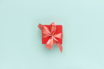 Red gift box with satin coral bow on top on a pastel turquoise background.