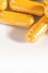 Macro close-up of randomly scattered turmeric capsules on a white background
