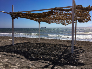 Mega gazebo craft structure on a beach in Kamari in Santorini, Greece. External structure on the shore of the Aegean Sea, in the distance on the horizon a large boat.