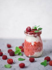 Raspberry cold summer cream dessert parfait on a grey table with mint