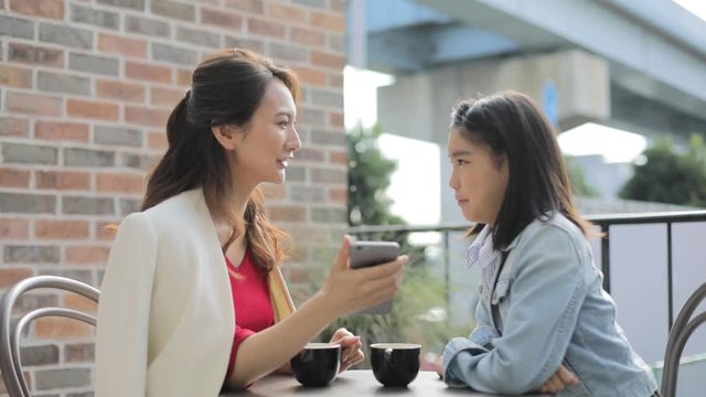 Mother and teenage daughter talking and looking at smartphone in cafe