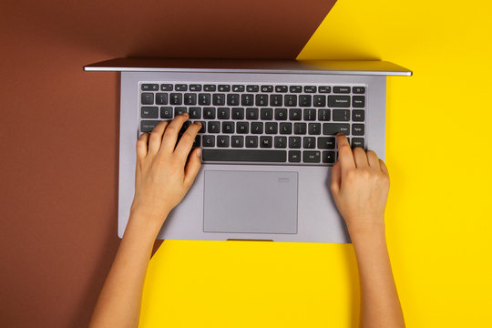 Kid Hands Typing On Laptop Computer Keyboard, Top View, Yellow And Brown Background