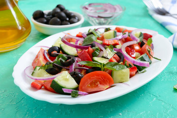 Tasty vitamin vegan salad of tomato, cucumber, red onion, black olives, basil sauce on a white plate on a bright background.