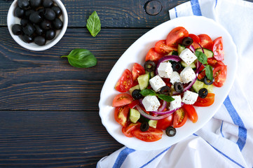 Tasty  vitamin salad with fresh vegetables, feta, black olives, basil sauce on a white plate on a wooden background. Top view