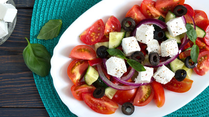 Tasty  vitamin salad with fresh vegetables, feta, black olives, basil sauce on a white plate on a wooden background. Top view.