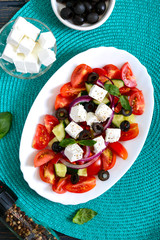 Tasty  vitamin salad with fresh vegetables, feta, black olives, basil sauce on a white plate on a wooden background. Top view.