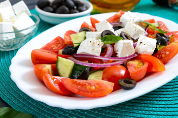 Tasty  vitamin salad with fresh vegetables, feta, black olives, basil sauce on a white plate on a wooden background.