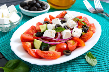 Tasty  vitamin salad with fresh vegetables, feta, black olives, basil sauce on a white plate on a wooden background.