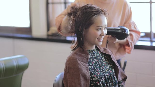Hairdresser drying hair of female customer with hair dryer