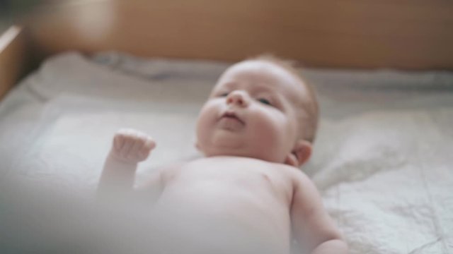adorable newborn boy with blond hair and plump cheeks lies on changing table and looks at nurse with interest closeup