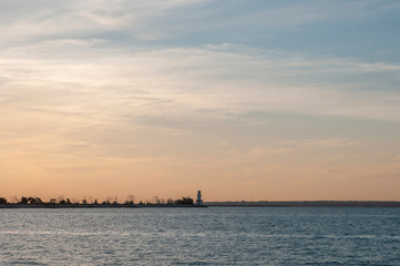 Obraz premium yellow sky and a distant lighthouse on a dam at sunset