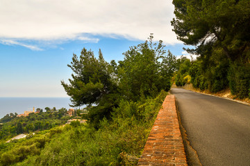 Fototapeta na wymiar High angle view from a panoramic road between Mediterranean vegetation on a hill leaned out on the sea with a small village in the background, Bussana, Imperia, Liguria, Italy