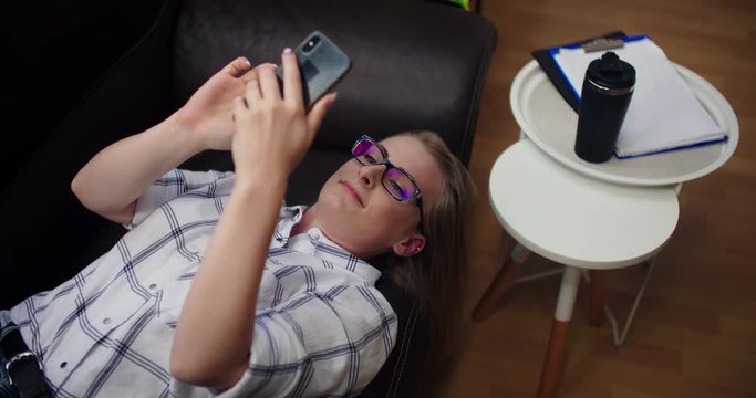 Attractive businesswoman having video call on mobile phone while lying on sofa at office